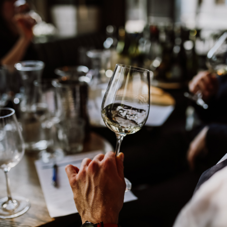 Close up of a hand holding a wine glass with white wine with a table in the background