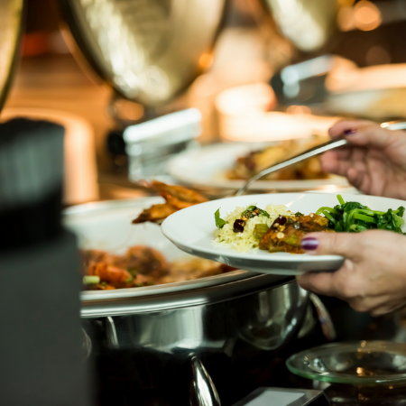 Hands holding a white plate serving food from a buffet