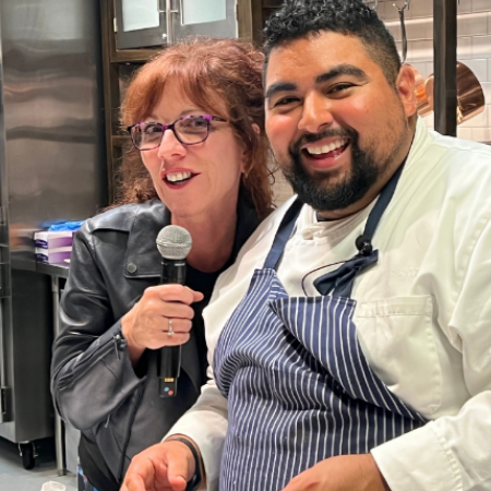 Woman with red hair holding a microphone next to a man in a blue striped apron